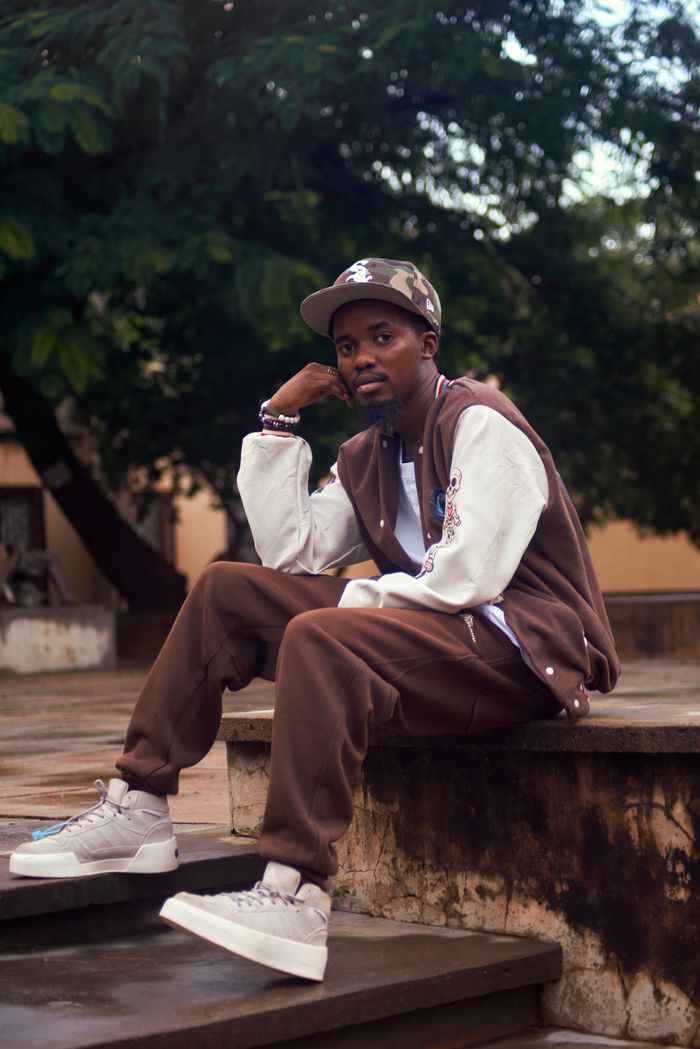 Young man in casual streetwear sits on stairs outdoors, showcasing urban fashion style.